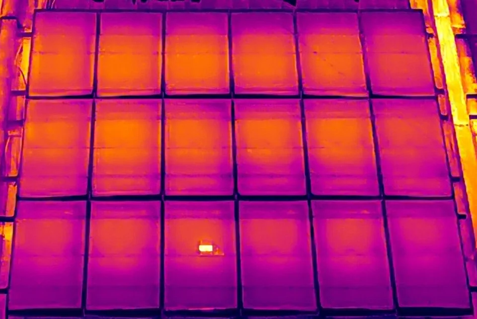 Aerial thermal image of an 18-module rooftop array; one module in the bottom row shows a small, bright hot area