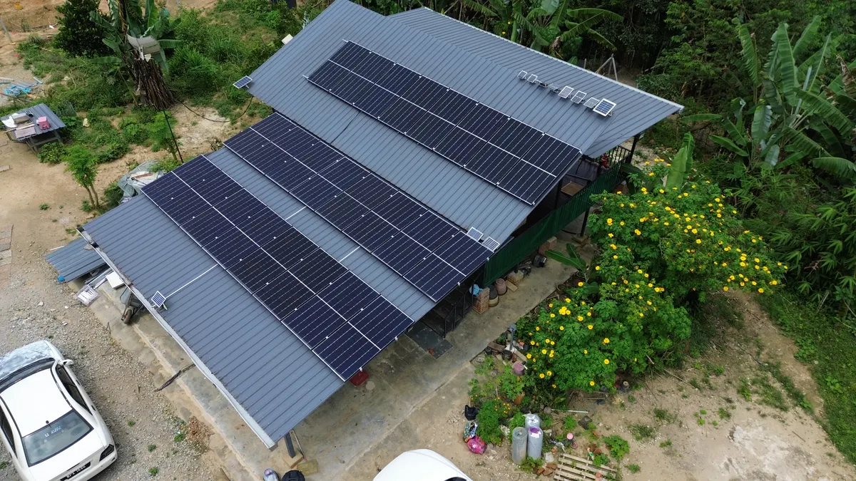 Aerial view of long rows of solar panels on a grey roof beside a garden