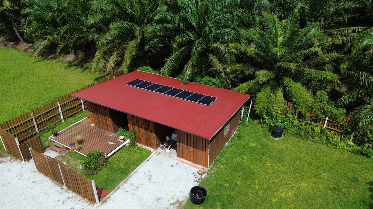 Aerial view of a wooden chalet with solar panels on its red roof among palm trees