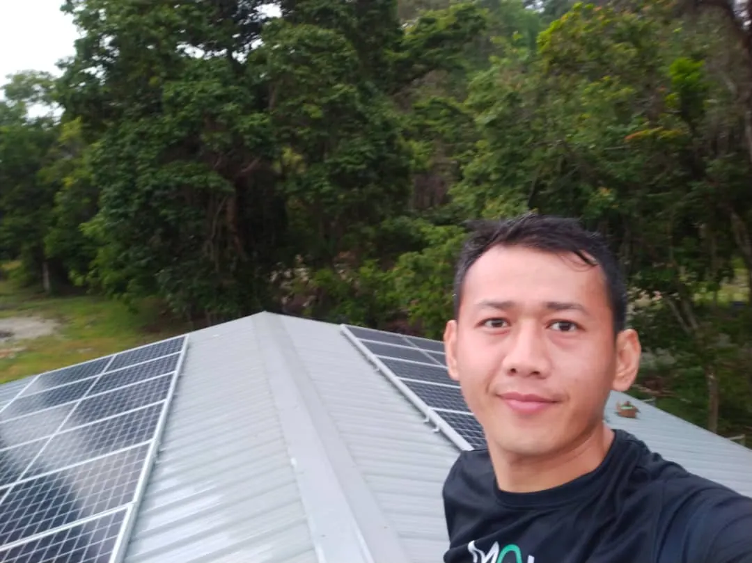 Jomsolar team member on site beside a rooftop solar array with forest behind
