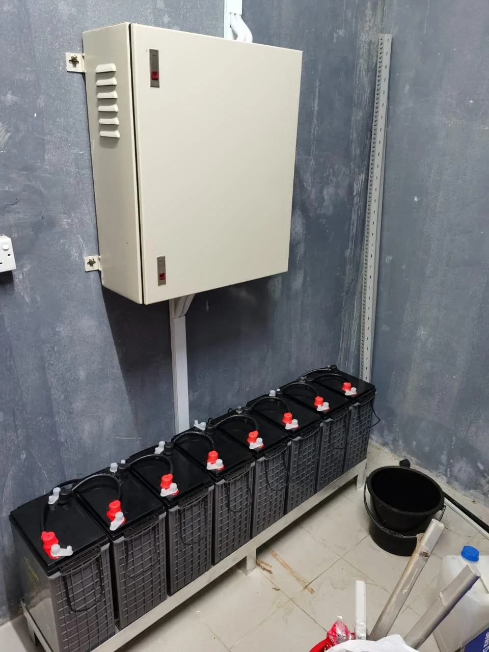 Electrical cabinet on the wall above a row of batteries in a battery room