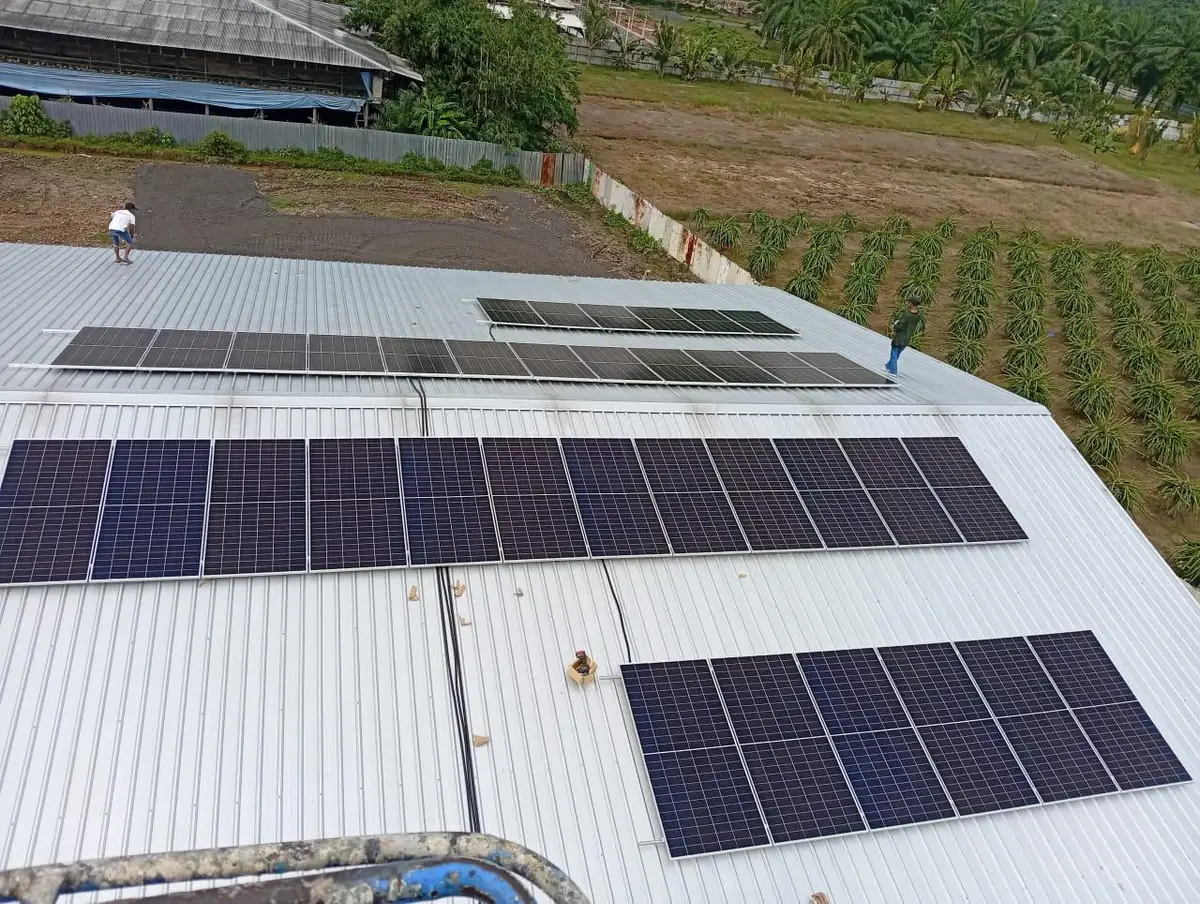 Aerial view of rows of solar panels on a large metal roof beside crop fields